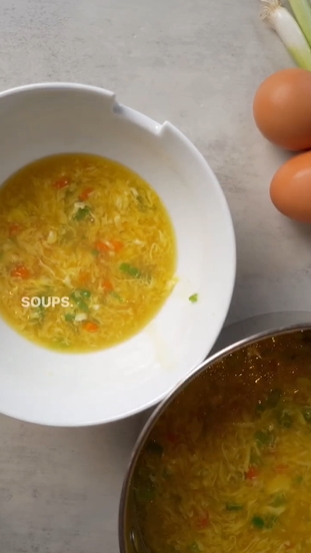 A bowl of soup with an egg in the background.