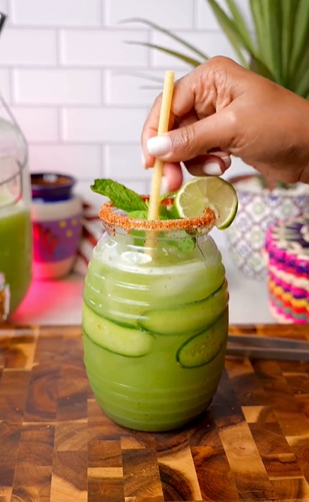 A person is drinking from a glass with cucumber and lime.