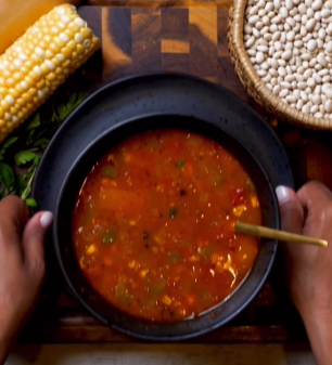 A bowl of soup with corn and beans on the side.