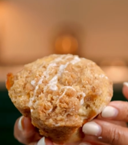 A person holding a muffin with icing on it.