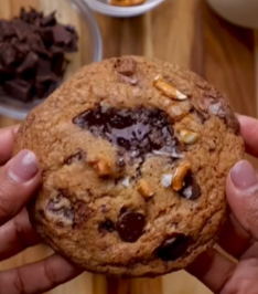 A person holding a chocolate chip cookie in their hands.