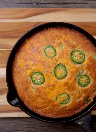 A jalapeno cornbread dish in a pan on top of a wooden table.