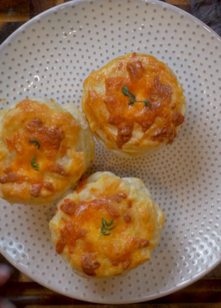 Three muffins with cheese and bacon on a plate.