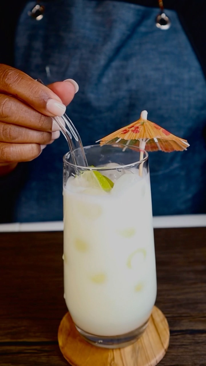 A person is holding a spoon in a glass of pina colada.