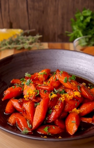 A bowl of carrots with orange and herbs.