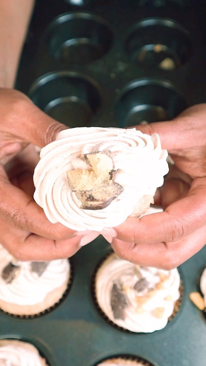 A person holding a cupcake with white frosting on it.