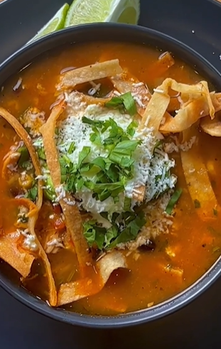 A bowl of soup with tortilla strips and rice.