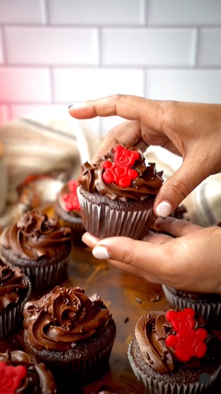 A person holding a cupcake with chocolate frosting.