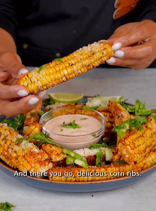 A person holding an ear of corn with sauce on it.