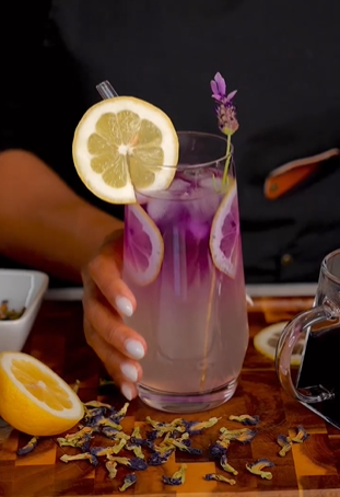 A person holding a glass of lemonade with lemon and lavender.