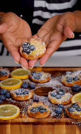 A person holding a donut with blueberries on top of it.