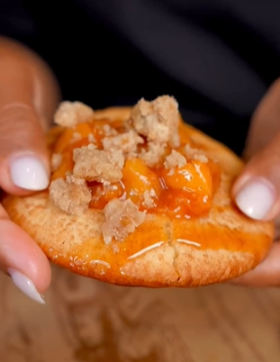 A person holding a cracker with cheese and meat.