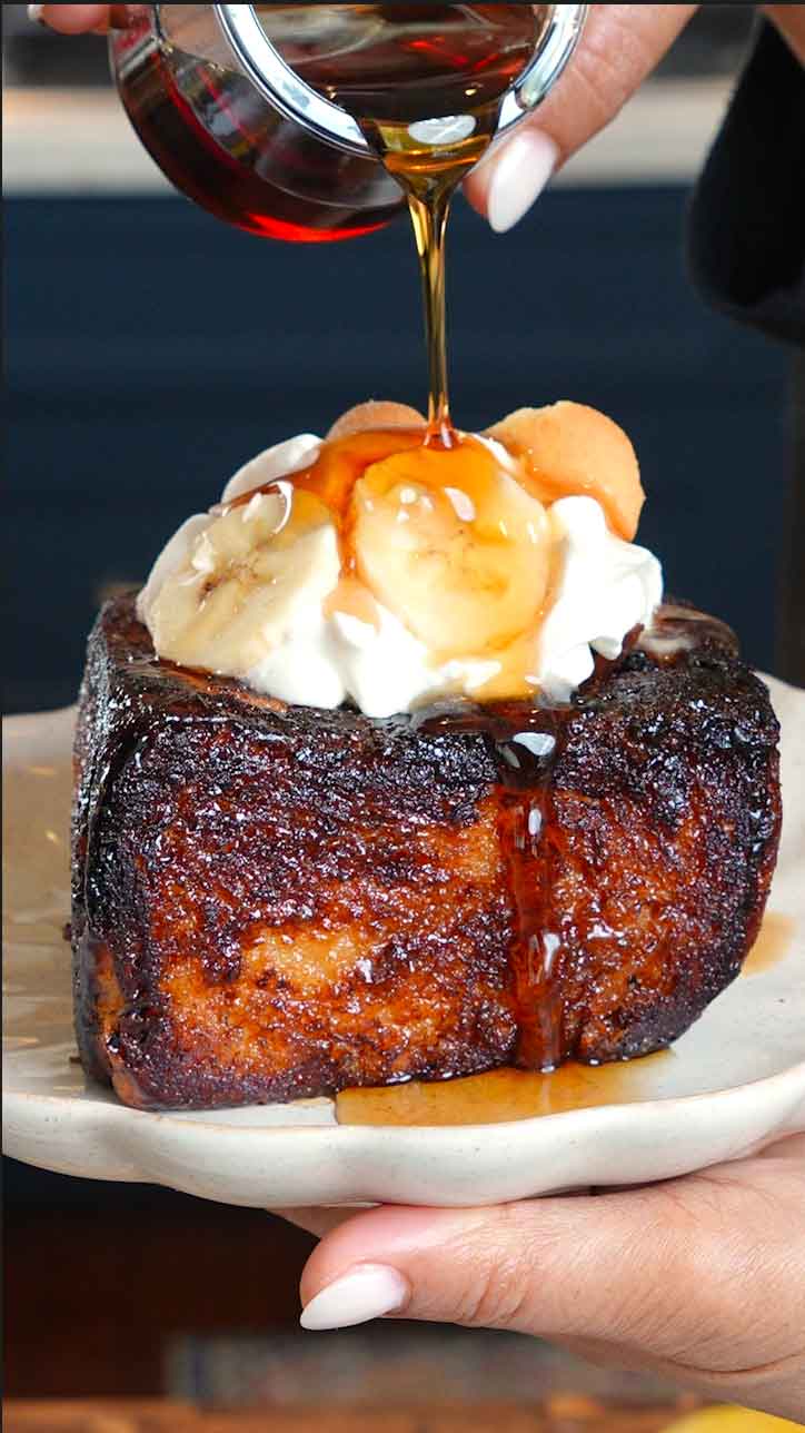 “Close-up of Shibuya banana pudding toast thick caramelized milk bread filled with creamy banana pudding and fresh banana slices, topped with whipped cream and maple syrup drizzle.